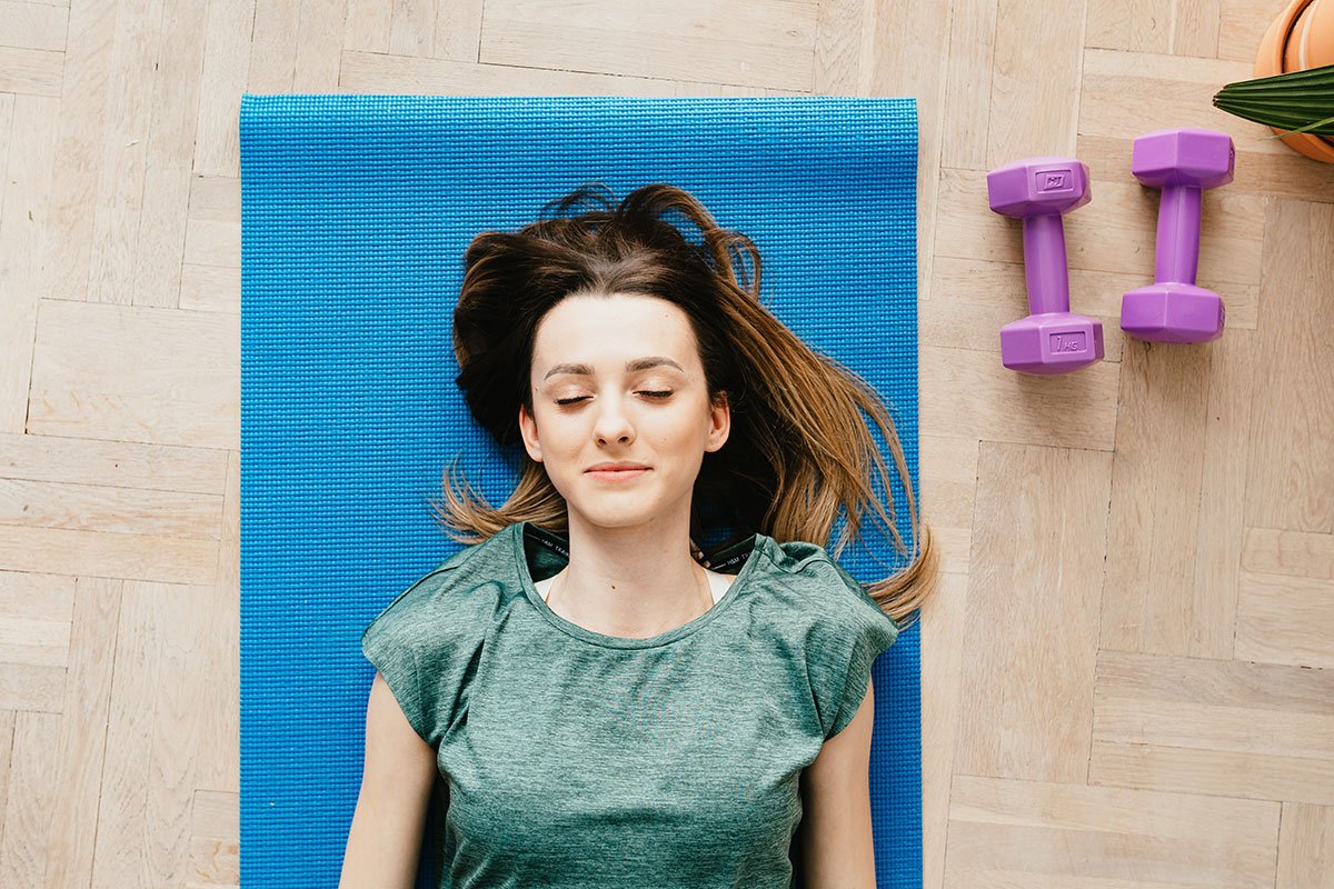 A lady lying on a yoga mat with her eyes shut and purple weights next to her