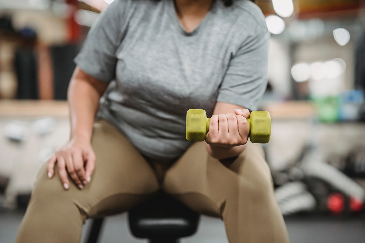 A person sat down lifting a green dumbbell in her left hand doing resistance exercises